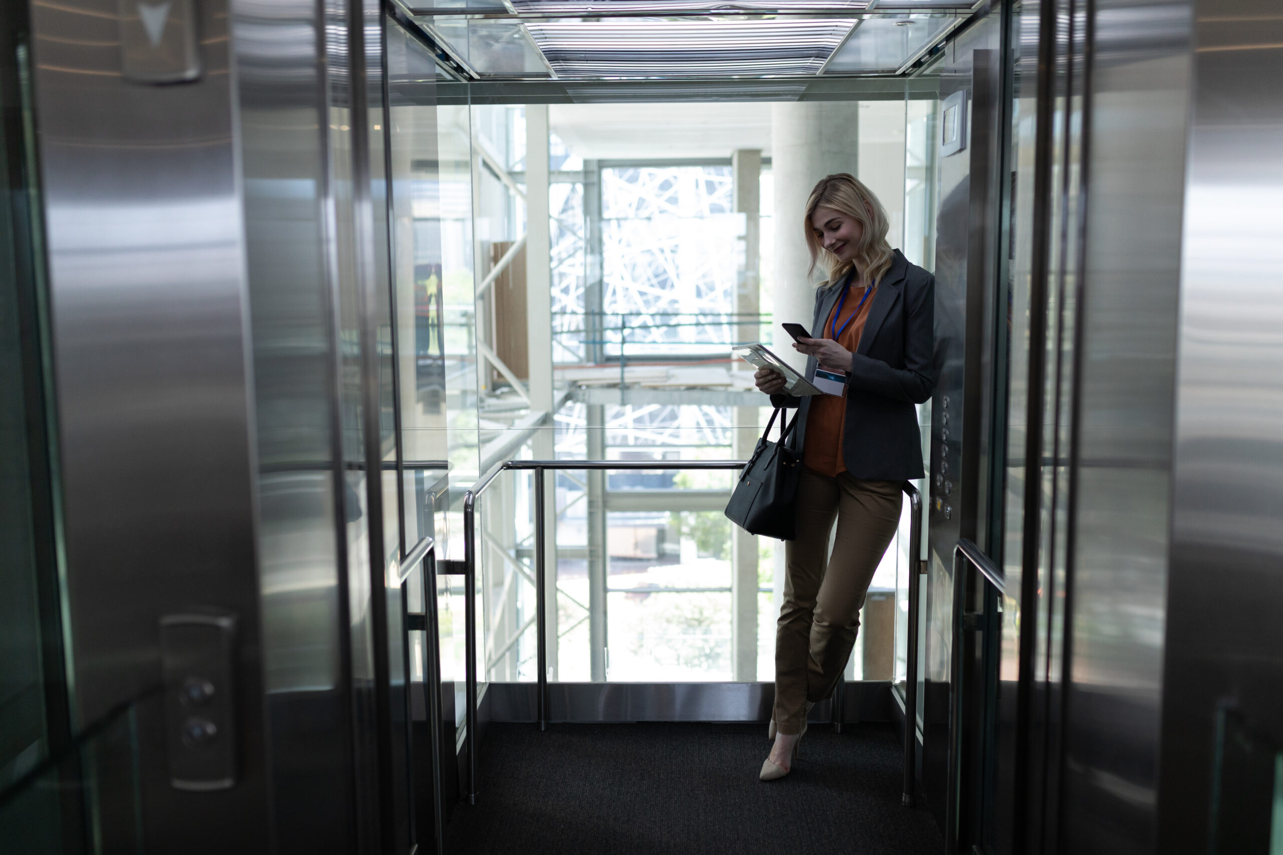 Blonde businesswoman using mobile phone in office elevator
